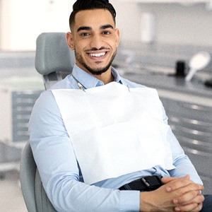 Bearded man smiling in dental chair with hands folded