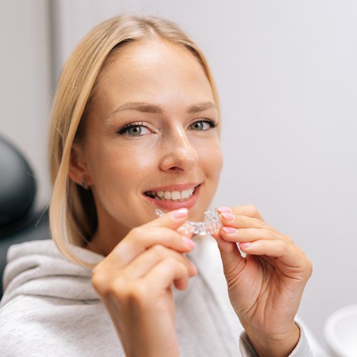 Woman smiling while holding clear aligner