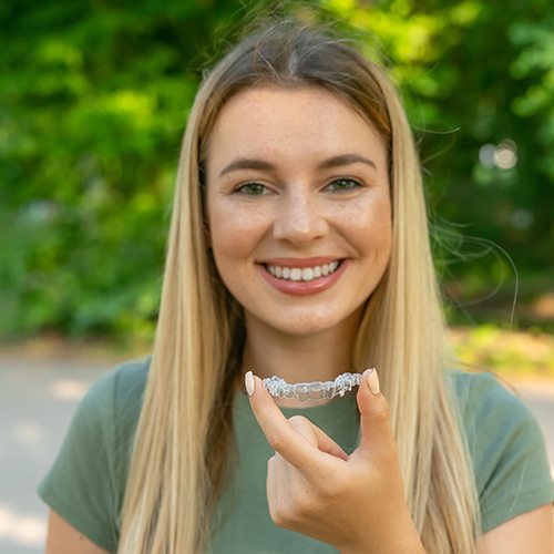 Woman in green shirt holding an Invisalign clear aligner