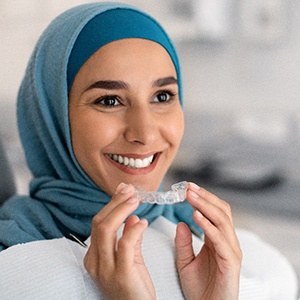 Woman sitting in dental chair holding clear aligner